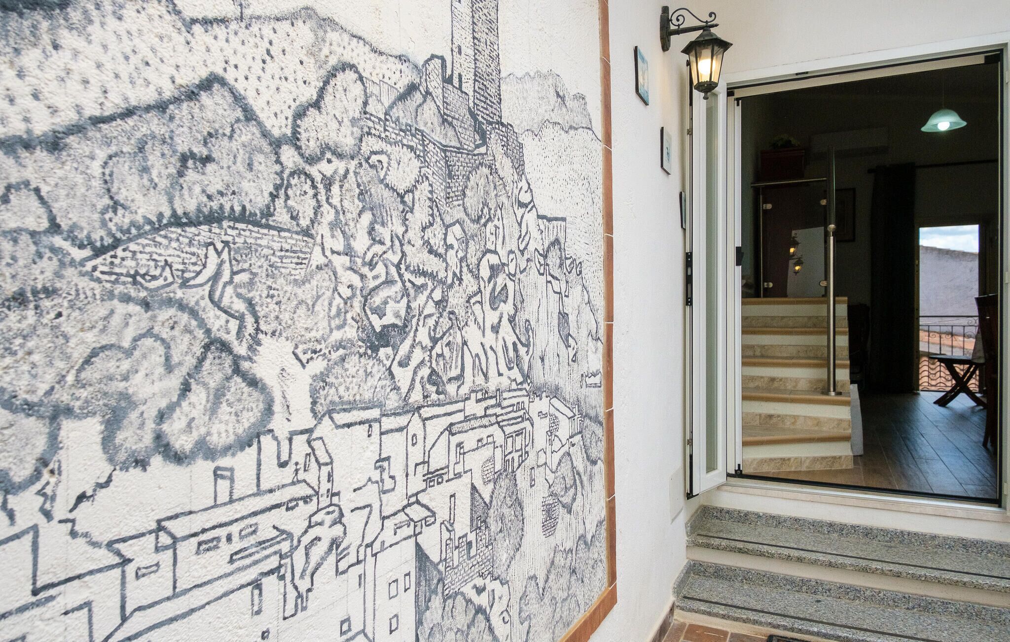 Ein detailliertes Schwarz-Weiß-Wandgemälde zeigt eine Stadt, eine Treppe, die zu einem Balkon führt, und eine Tür mit einer Leuchte.