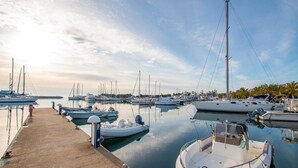 Een jachthaven met verschillende boten die aanmeren, een betonnen steiger en stilstaand water dat de boten weerspiegelt.