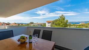 A balcony with a wooden table, two chairs, a bottle of champagne, and a bowl of fruit. - 1 bedroom amazing apartment in Bibinje (Bibinje)