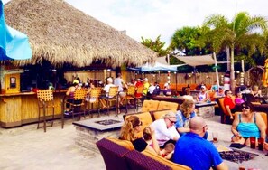 An outdoor bar area with thatched roofs, wicker furniture, and a poolside setting.