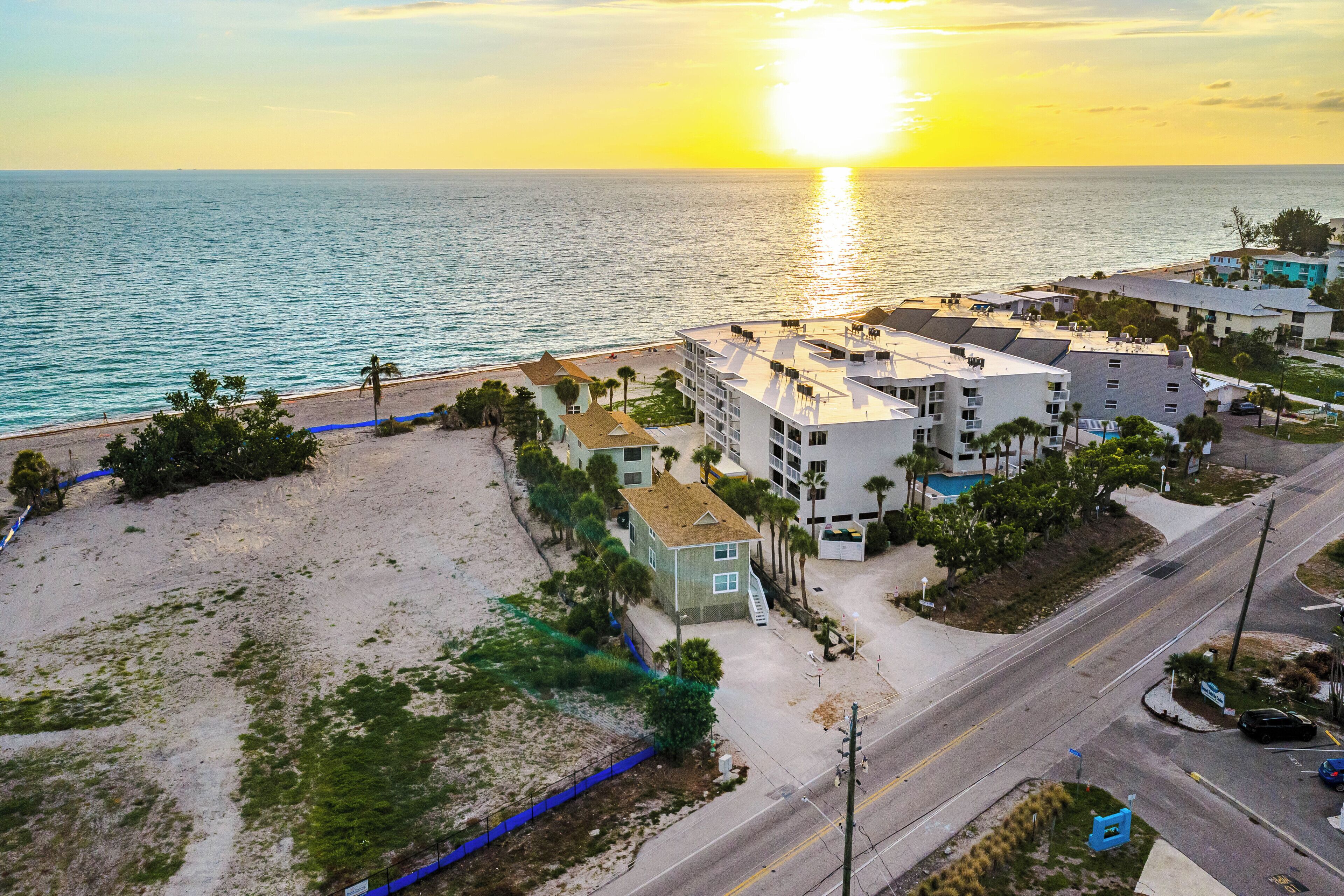 A coastal hotel with multiple buildings, a beach, and a road.