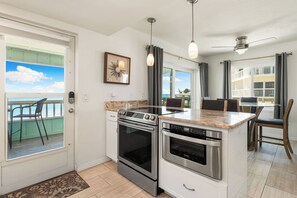 A modern kitchen with stainless steel appliances, a marble countertop, and a view of the ocean through large windows.