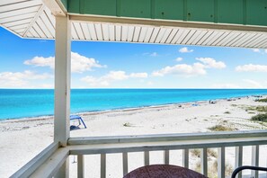 Blick auf einen Strand von einer überdachten Veranda bei blauem Himmel und ruhiger See.