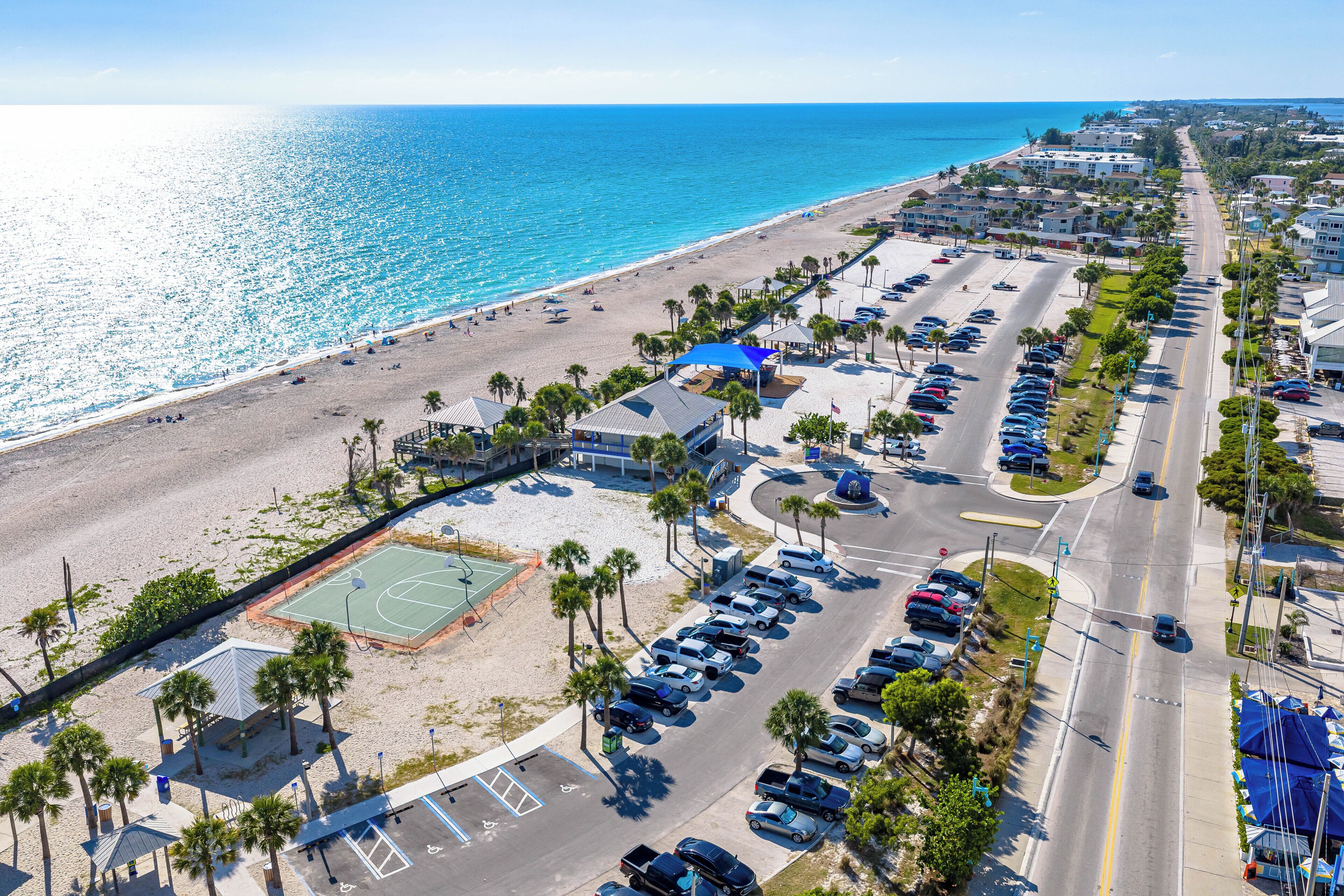 Vue aérienne d’une zone côtière avec une plage, un parking et des bâtiments.