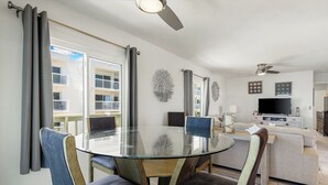 Ein modernes Wohnzimmer mit einem Glastisch, bequemen Sitzmöglichkeiten, einem Flachbildfernseher und einem Balkon mit Blick auf ein Gebäude.