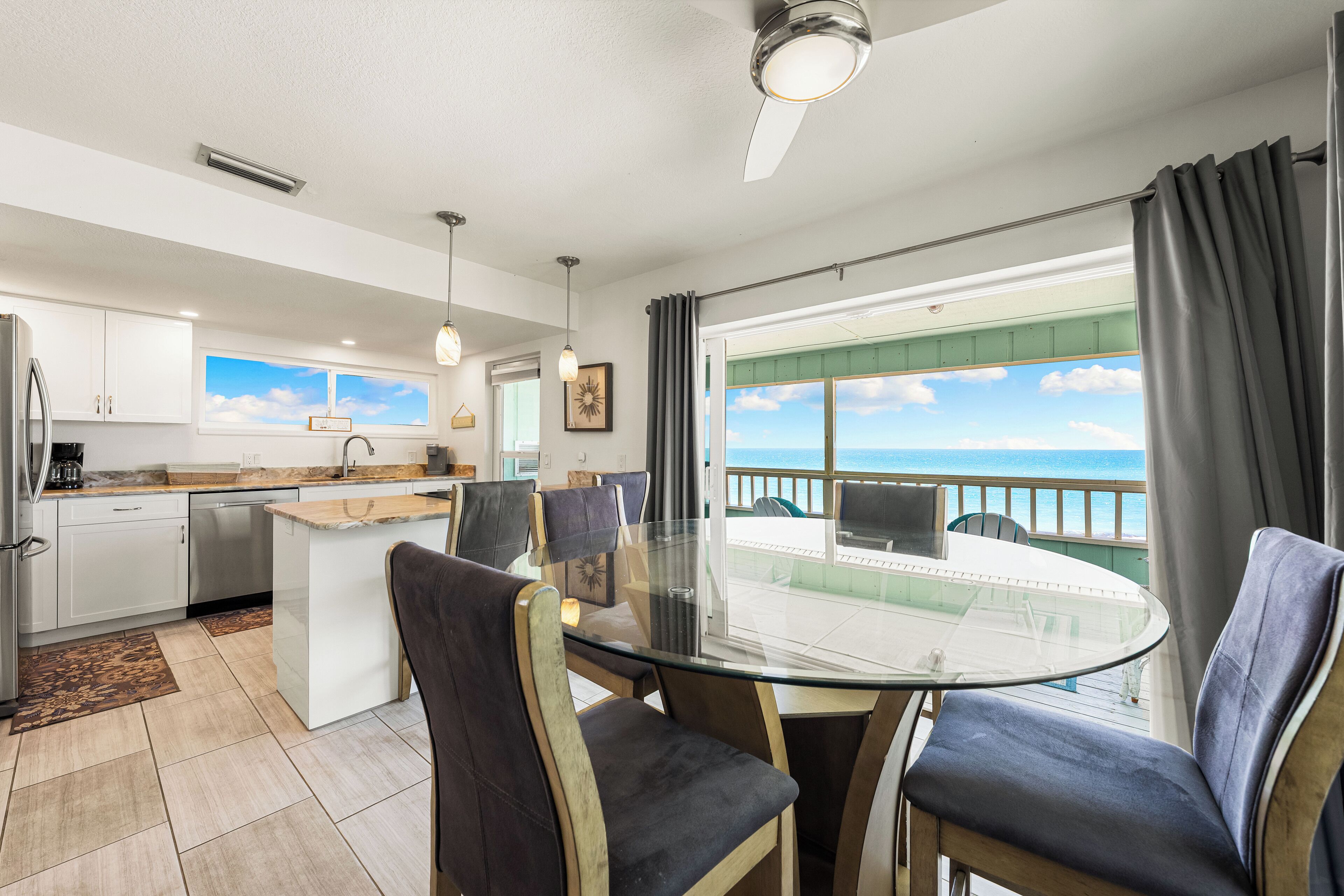 A modern kitchen with white cabinets, a dining area with a glass table, and a view of the ocean.