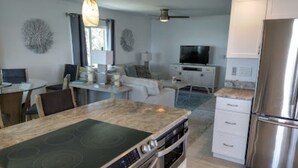 Una cocina moderna con estufa, horno y refrigerador integrados, comunicada con un comedor que tiene una mesa y sillas.