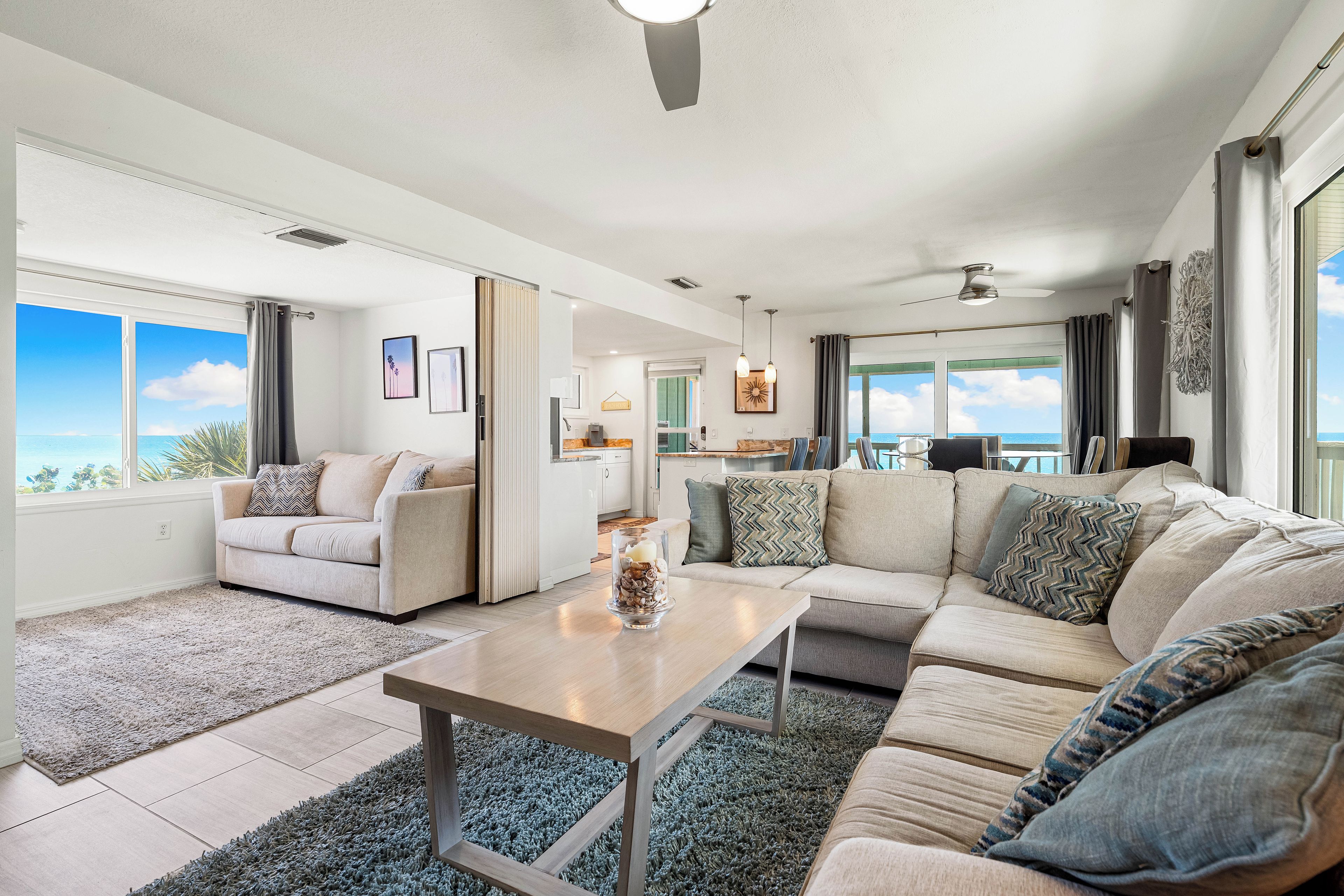 A spacious living room with a large sofa, a coffee table, and a view of the ocean.