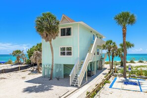 A two-story beach house with a balcony, a staircase, and a view of the ocean.