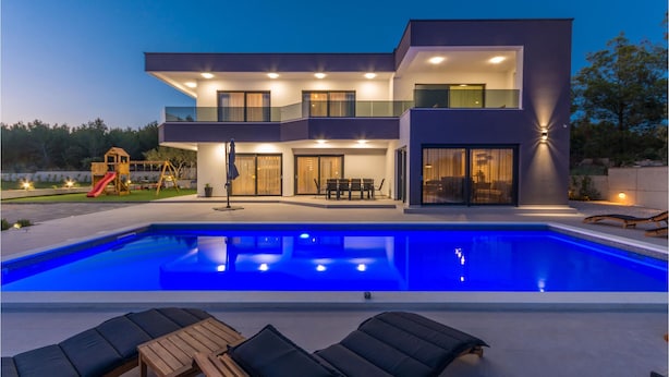 Een modern huis met twee verdiepingen, een zwembad, terras en een speelruimte.