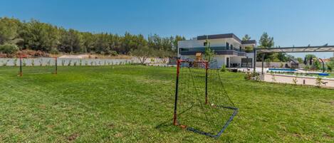Un espacio al aire libre con césped, un arco de fútbol y un edificio moderno al fondo.