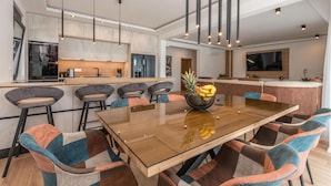 Een moderne keuken met een centraal eiland, barstoelen en een eettafel met een fruitschaal.