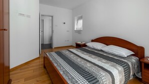 A bedroom with a wooden bed, a nightstand, a bedside table, and a window with blinds. - 2 bedroom awesome apartment in Crikvenica (Crikvenica)
