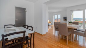 A modern dining area with a wooden table and chairs, a grey cabinet, and a view of the cityscape through large windows. - 2 bedroom awesome apartment in Crikvenica (Crikvenica)