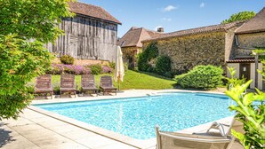 Una piscina con sillones de descanso y un edificio de madera al fondo.