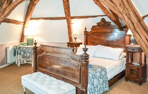 Un lit traditionnel en bois à baldaquin, avec un banc recouvert d’un tissu blanc, deux tables de chevet avec des lampes et un radiateur.