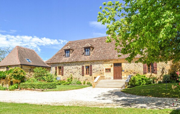 Une maison en pierre au design traditionnel, dotée d’une entrée avec des marches, d’un petit porche et d’une allée gravillonnée.