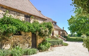 Un bâtiment en pierre doté d’un toit en pente, d’une allée gravillonnée et d’une végétation luxuriante.