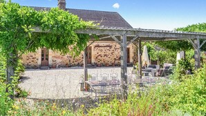 Un edificio de piedra con un patio cubierto, mobiliario exterior y una pérgola con enredaderas.