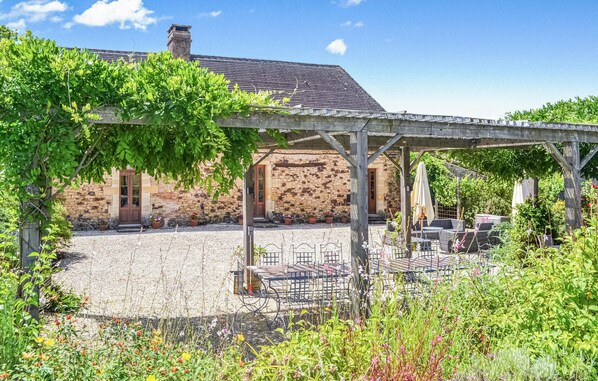 Ein Steinhaus mit überdachter Terrasse, Sitzgelegenheiten im Freien und einer Pergola mit Weinreben.