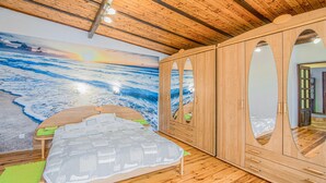 Ein Zimmer mit Holzbalkendecke, einem Bett mit weißer Bettdecke, einem großen Spiegel und einem Wandbild mit Strandmotiv.