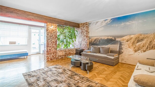 Ein geräumiges Wohnzimmer mit einer Wand aus Stein, einem großen Fenster, einer Couch, einem Couchtisch und einem gemusterten Teppich.