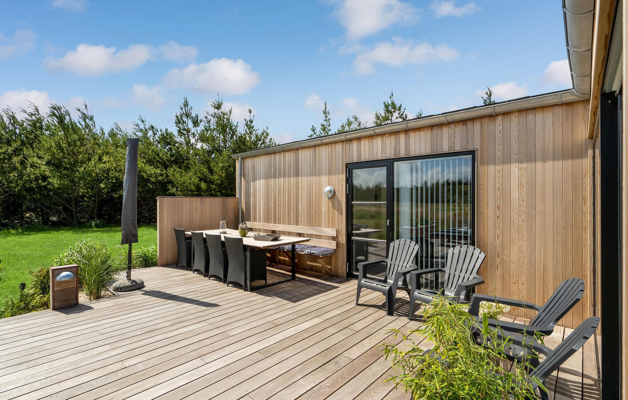 Une terrasse en bois avec une table et des chaises, une porte vitrée et une vue sur un paysage verdoyant.