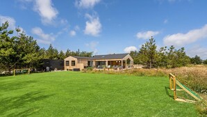 A modern house with a large lawn, a wooden deck, and a swing set.