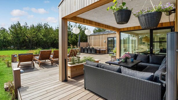 A covered outdoor deck with wooden furniture, a dining area, and hanging planters.