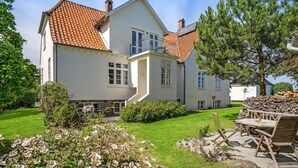 Ein zweistöckiges Haus mit Ziegeldach, einem Balkon und einem gepflegten Garten mit Blumen und einem Holztisch.