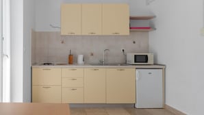 Une cuisine compacte avec des meubles de couleur beige, un évier blanc, un four à micro-ondes et un petit réfrigérateur.