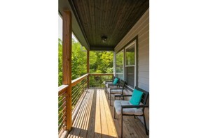 Relax on the outdoor space with a seating area featuring three chairs and a railing overlooking lush greenery.