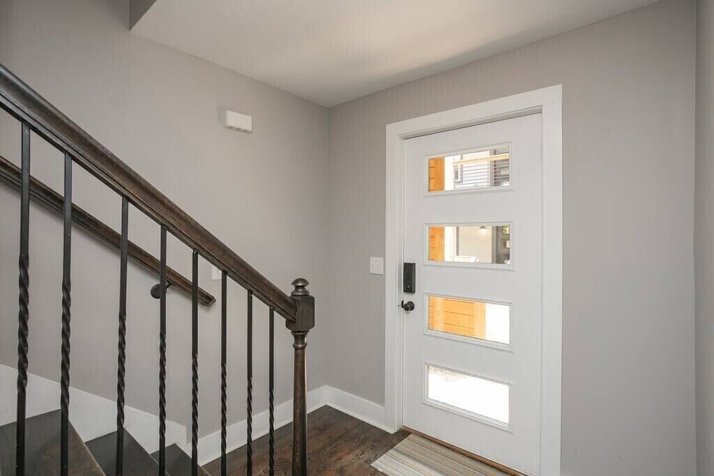 A staircase with a wooden handrail and dark steps leading to a white door with three windows.