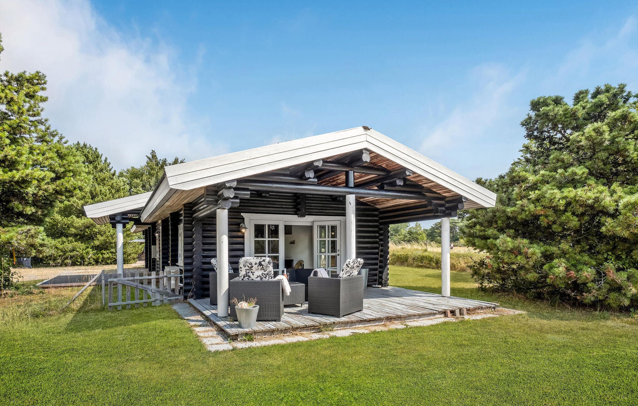 A log cabin with a covered porch, outdoor seating, and a view of the surrounding forest.