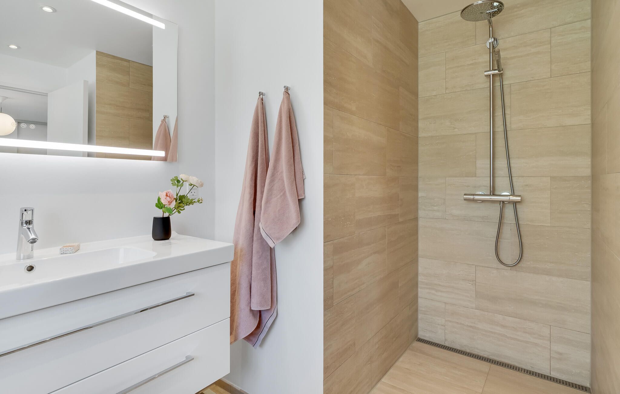 A modern bathroom with a white vanity, a large mirror, and a shower with a handheld showerhead.