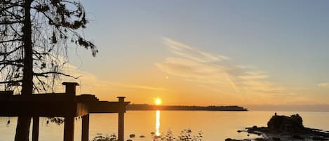 A wooden deck overlooking a calm body of water with a sunset in the background.
