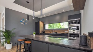 Una cocina moderna con una isla central, hornos integrados y un amplio ventanal.