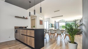 Una cocina moderna con armarios de madera, una isla central, iluminación colgante y un comedor con un ventanal grande.