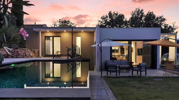 Una casa moderna con piscina, mobiliario exterior y un patio bien iluminado.