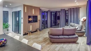 Una sala de estar moderna con un sofá modular, una mesa de comedor y un televisor montado en una pared de paneles de madera.