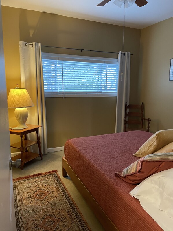 A bedroom with a bed, a nightstand, a lamp, a chair, and a window with blinds.