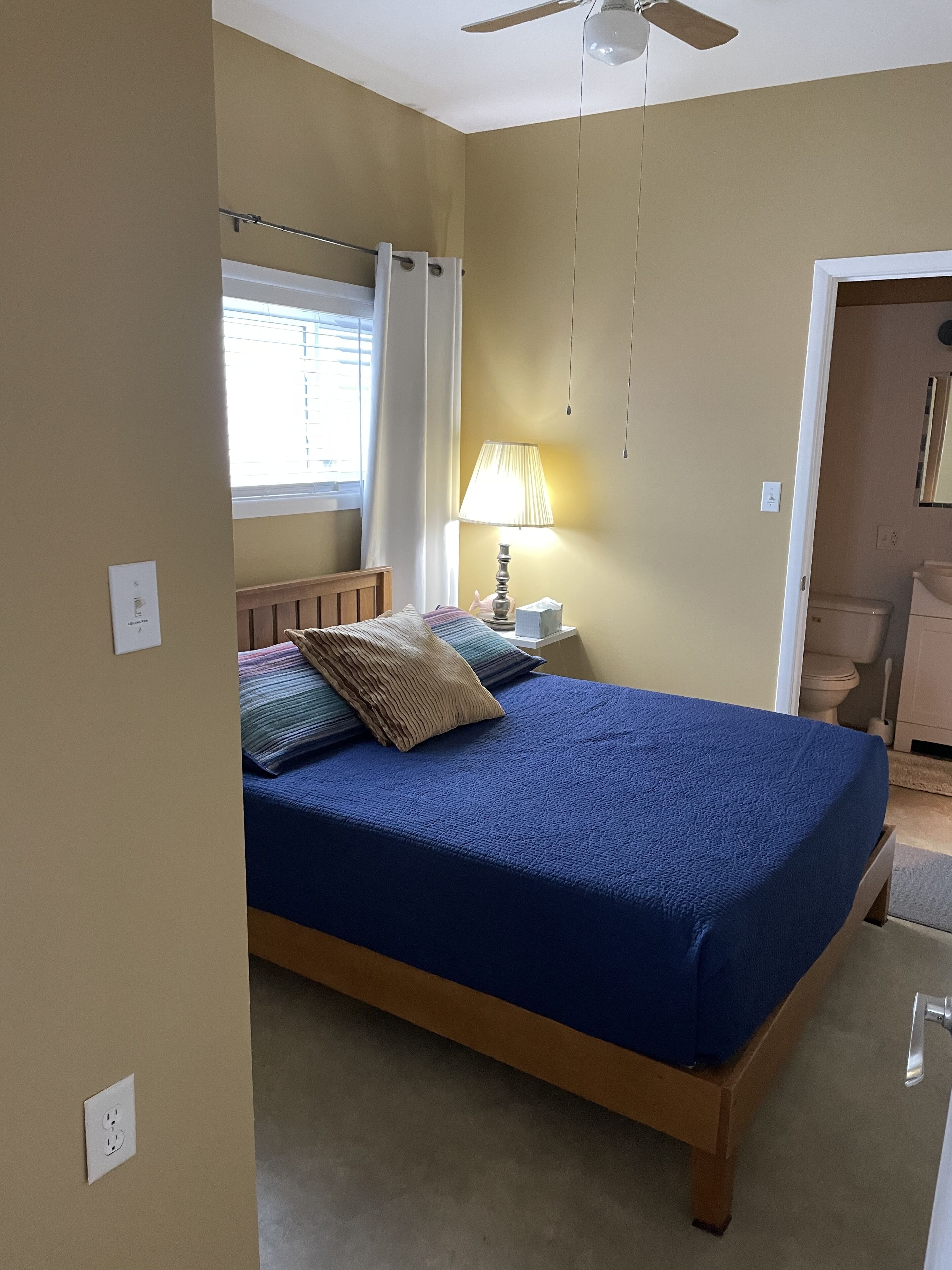 A bedroom with a bed, a nightstand, a lamp, a window with curtains, and a ceiling fan.