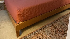 A bedroom with a wooden bed, beige walls, and a patterned rug. - Shore Cliff Cottage  (Ashtabula)