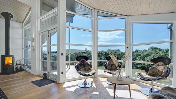 A modern interior with a large glass door leading to an outdoor deck, a wood-burning stove, and three cat chairs with decorative items. - Stunning home in Hjørring with WiFi (Hjørring)