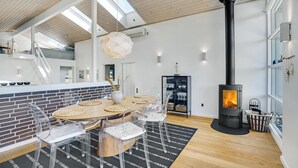 A modern kitchen with a central island, a dining area with a round table and chairs, a large window, and a wood-burning stove. - Stunning home in Hjørring with WiFi (Hjørring)