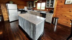 Une cuisine avec des murs en bois, un îlot central doté d’un comptoir en granit, des appareils électroménagers en acier inoxydable et une vue sur l’extérieur.