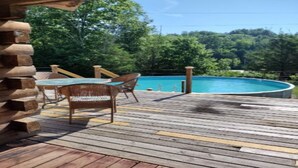 Une terrasse en bois avec une piscine, entourée d’arbres.