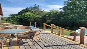Une terrasse en bois avec une table ronde et des chaises, une piscine et une rambarde en bois.