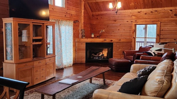 L’intérieur d’un chalet confortable, avec une cheminée, des meubles en cuir et un téléviseur.