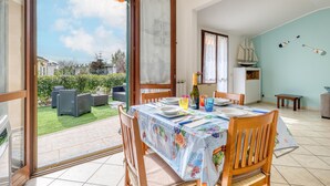 Un coin repas avec une table dressée pour quatre personnes, une bouteille de champagne et une vue sur un jardin et la mer, grâce à des portes ouvertes.